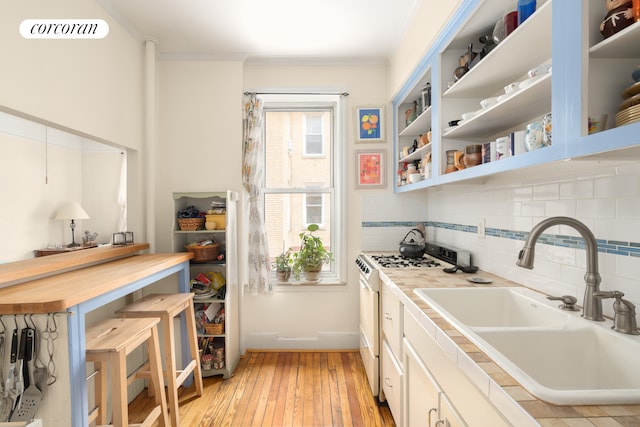 kitchen featuring a sink, light wood-style floors, tasteful backsplash, and white gas stove