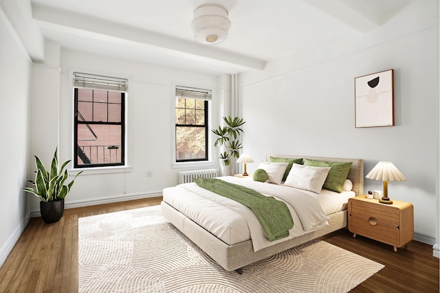 bedroom with wood finished floors, baseboards, radiator heating unit, and beamed ceiling