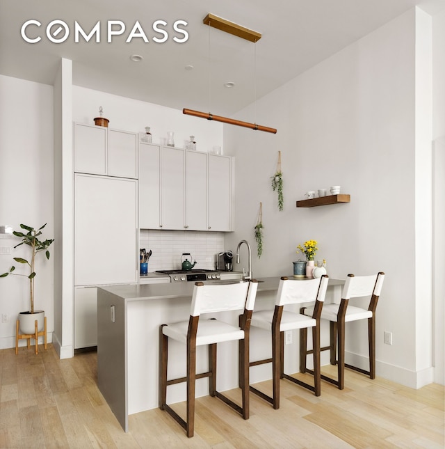 kitchen with a peninsula, a kitchen breakfast bar, white cabinets, light wood-style flooring, and backsplash