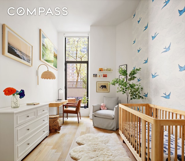 bedroom featuring a nursery area, wallpapered walls, and light wood finished floors