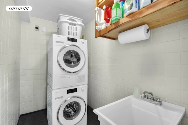 laundry room featuring laundry area, a sink, stacked washer / drying machine, and tile walls