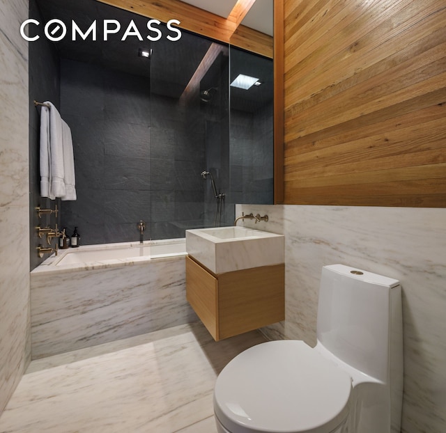 bathroom featuring walk in shower, vanity, toilet, a tub with marble appearance, and tile walls