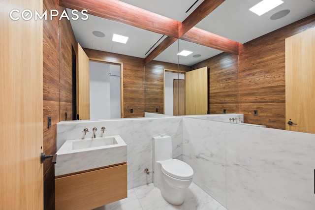 bathroom featuring vanity, wood walls, marble finish floor, beam ceiling, and toilet