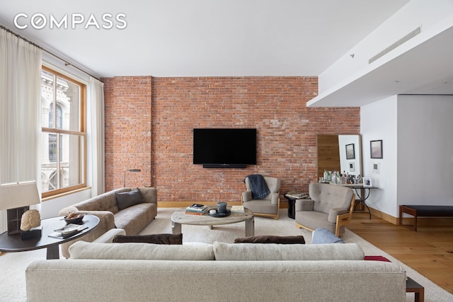 living area featuring baseboards, brick wall, and wood finished floors