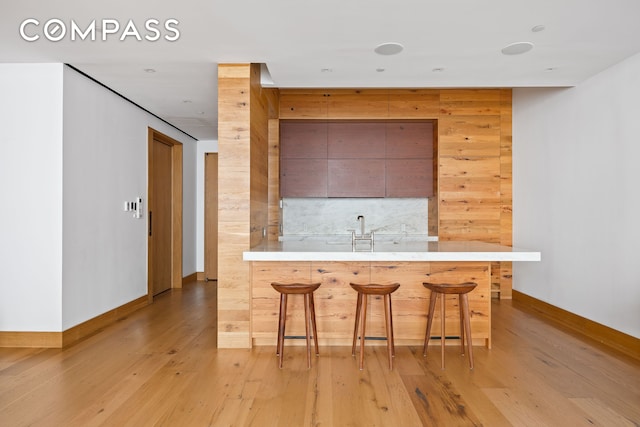 kitchen featuring decorative backsplash, a kitchen breakfast bar, light countertops, baseboards, and light wood-style floors