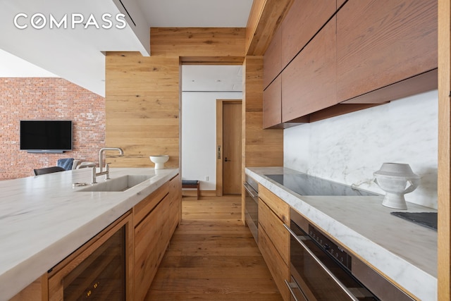 kitchen with wood walls, wood finished floors, beverage cooler, black electric cooktop, and a sink