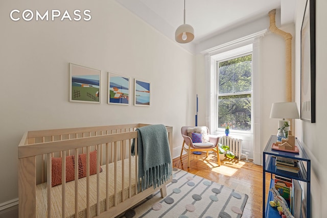 bedroom with radiator, baseboards, a nursery area, and wood finished floors