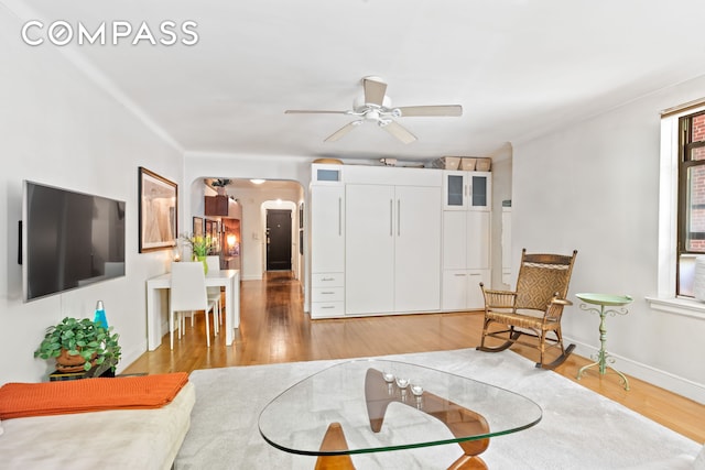 living room featuring light wood-style floors, arched walkways, baseboards, and ceiling fan