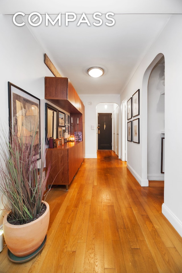 hallway with arched walkways, baseboards, and light wood-type flooring
