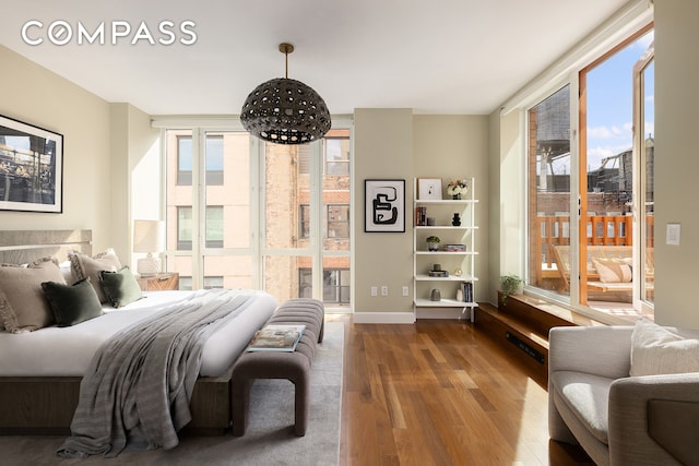bedroom featuring floor to ceiling windows, multiple windows, wood finished floors, and access to exterior