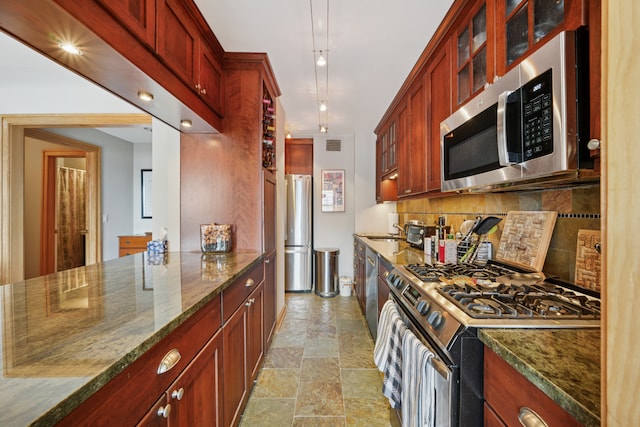 kitchen with glass insert cabinets, dark stone counters, stone finish flooring, backsplash, and stainless steel appliances