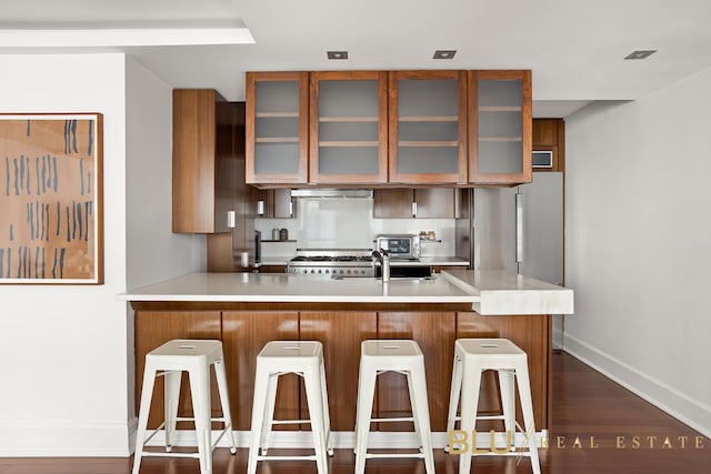 kitchen with exhaust hood, appliances with stainless steel finishes, light countertops, a peninsula, and baseboards
