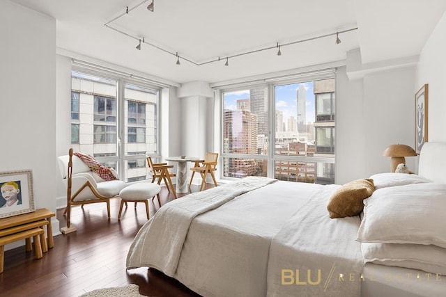 bedroom with a view of city, rail lighting, and dark wood finished floors