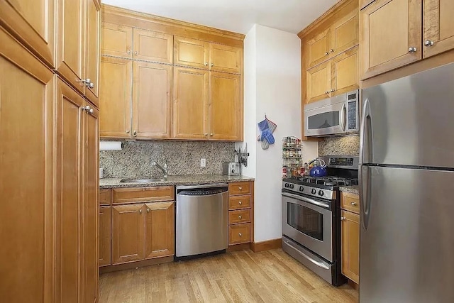 kitchen featuring backsplash, light wood-type flooring, a sink, dark stone countertops, and stainless steel appliances