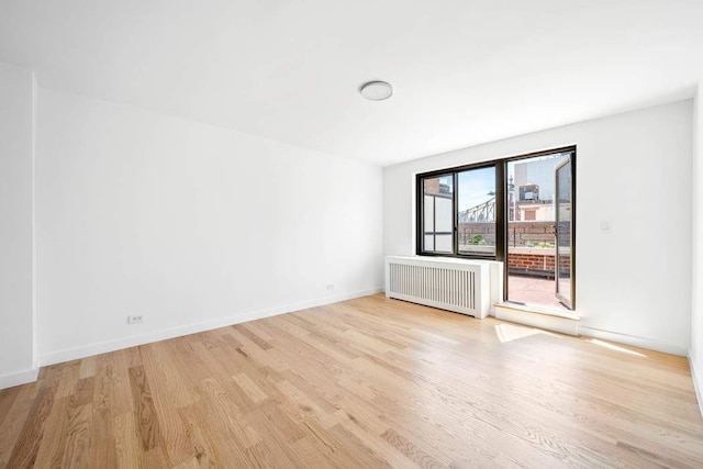 spare room featuring baseboards, radiator heating unit, and light wood-style flooring