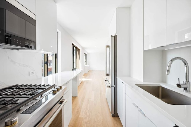 kitchen with modern cabinets, light wood-type flooring, white cabinets, a sink, and stainless steel appliances
