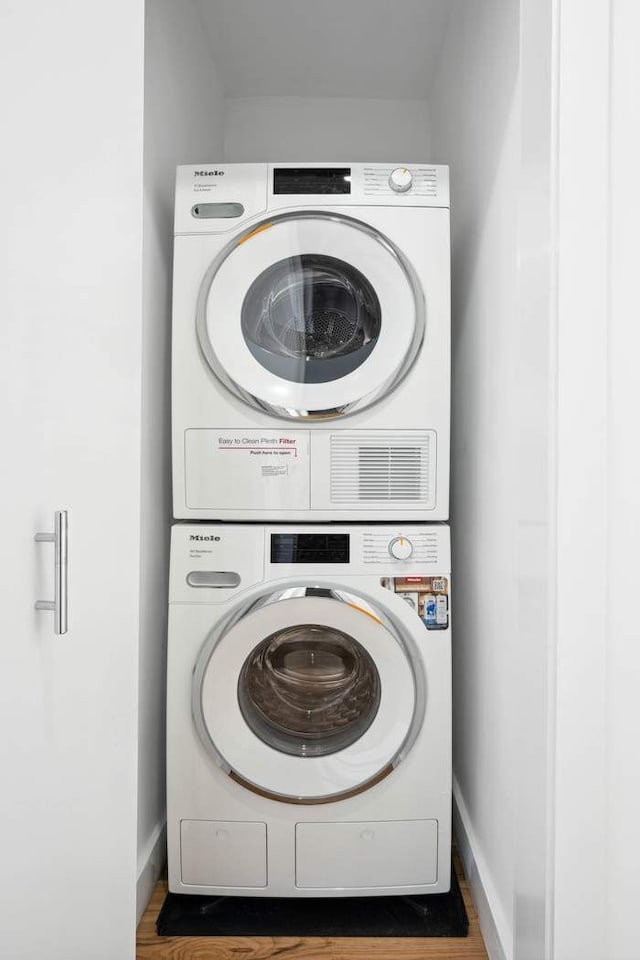 laundry room featuring laundry area, stacked washer and dryer, baseboards, and wood finished floors