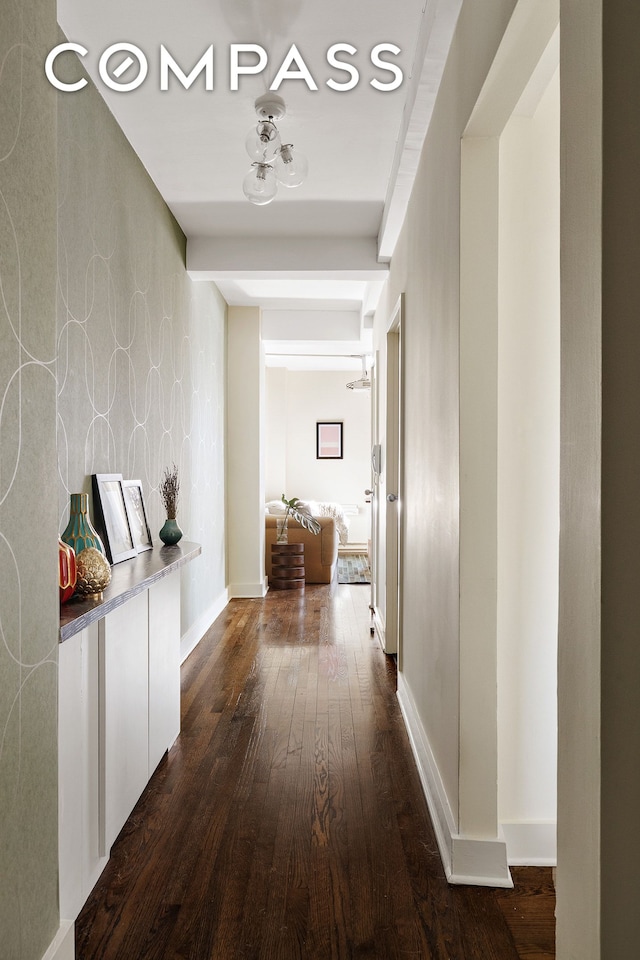 hallway featuring wallpapered walls, baseboards, and dark wood-type flooring