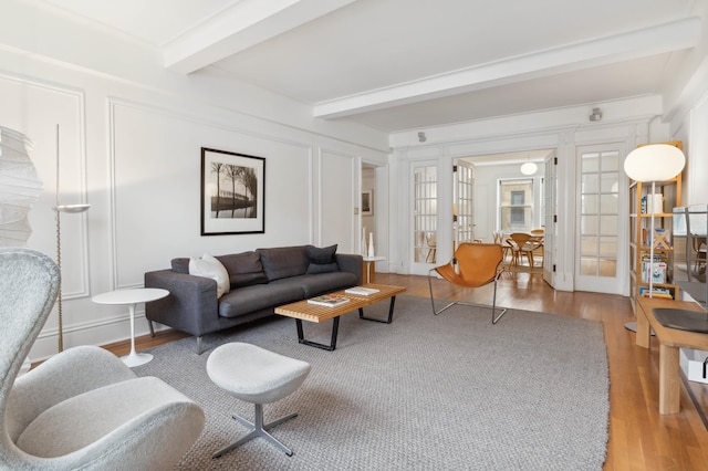 living area with beamed ceiling, french doors, light wood-style flooring, and a decorative wall