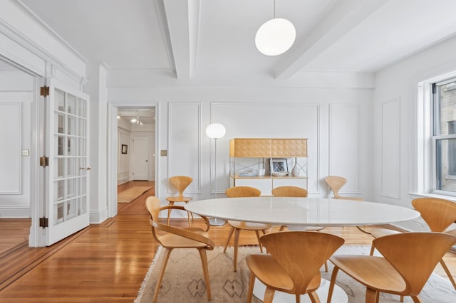 dining area featuring beamed ceiling, a decorative wall, and wood finished floors