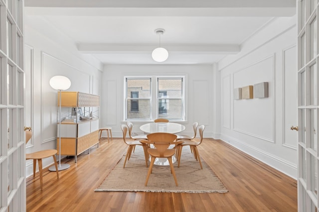 dining area featuring a decorative wall, light wood-type flooring, and beam ceiling