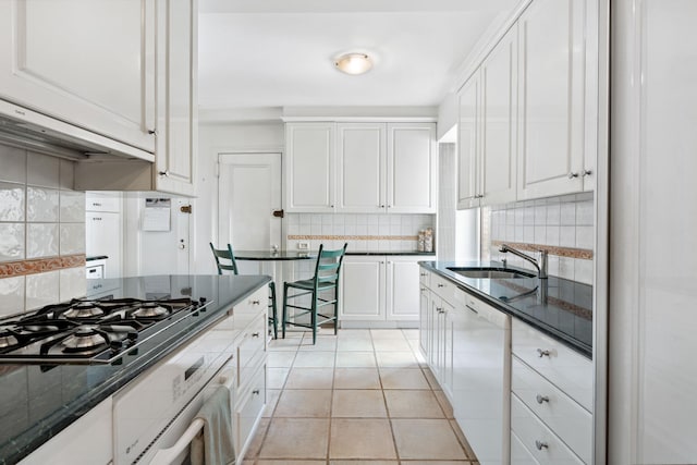 kitchen with tasteful backsplash, a sink, light tile patterned floors, white appliances, and white cabinetry