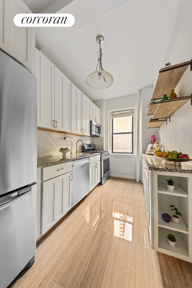 kitchen featuring stainless steel appliances, open shelves, backsplash, dark stone counters, and white cabinetry