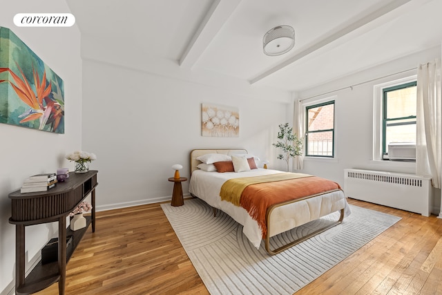 bedroom with radiator heating unit, light wood-style flooring, beamed ceiling, and baseboards