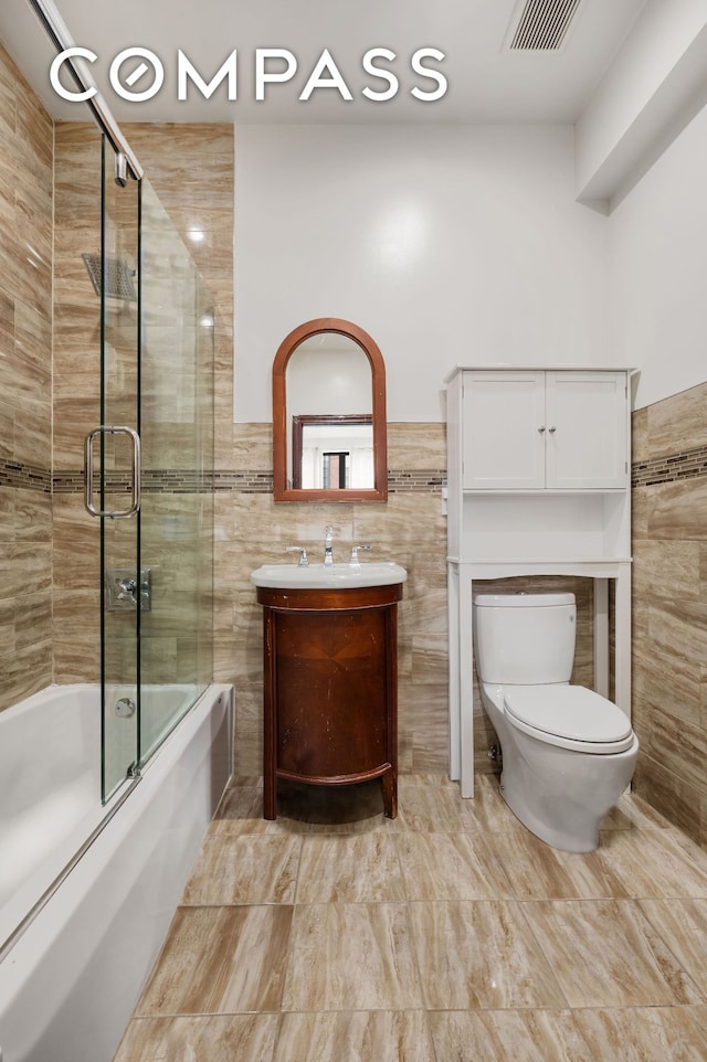 475 W 146th St, New York City, NY 10031 - bathroom featuring tile walls, toilet, shower / bath combination with glass door, vanity, and a wainscoted wall