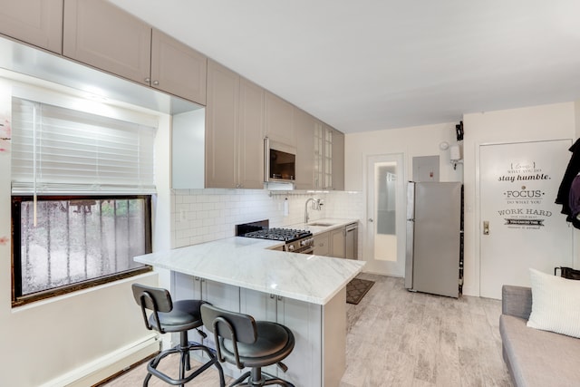 kitchen featuring tasteful backsplash, light stone countertops, a sink, a breakfast bar, and stainless steel appliances
