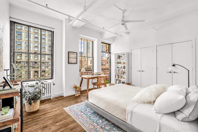 bedroom featuring radiator, wood finished floors, two closets, baseboards, and a ceiling fan