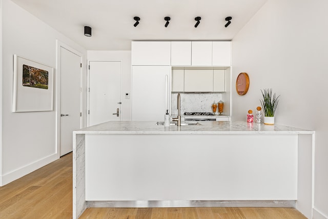kitchen with light stone countertops, a sink, white cabinetry, light wood-type flooring, and tasteful backsplash