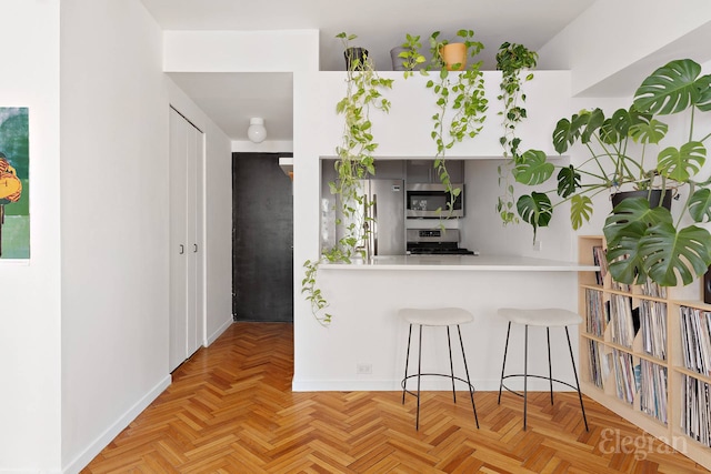 kitchen with a sink, a breakfast bar area, light countertops, stainless steel appliances, and baseboards