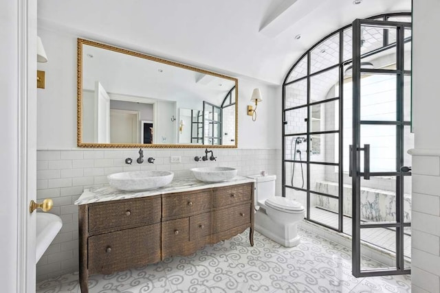 bathroom featuring toilet, tile patterned floors, tile walls, and a sink