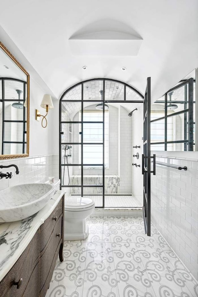 bathroom with vanity, toilet, a wainscoted wall, tile walls, and tiled shower