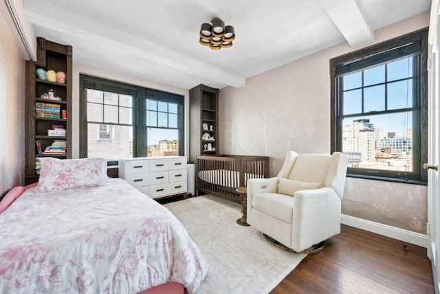 bedroom featuring baseboards, multiple windows, wood finished floors, and beam ceiling