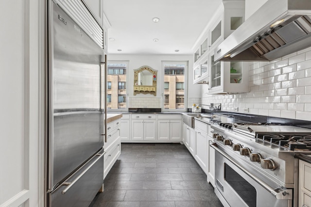 1 E End Ave Unit 8A, New York City, NY 10075 - kitchen featuring premium appliances, wall chimney range hood, a sink, backsplash, and white cabinetry