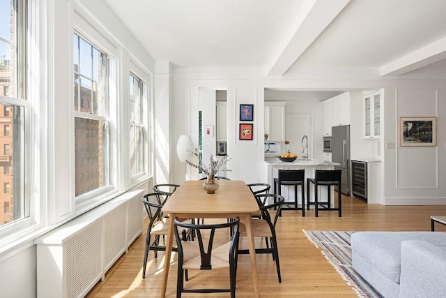 dining room with beverage cooler, plenty of natural light, light wood finished floors, and radiator