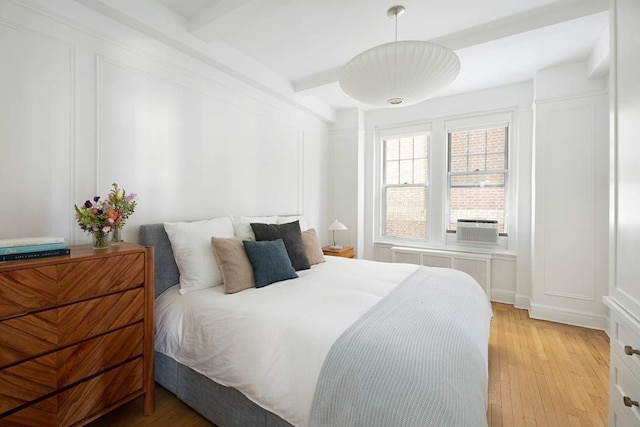 bedroom featuring radiator heating unit, a decorative wall, and light wood finished floors