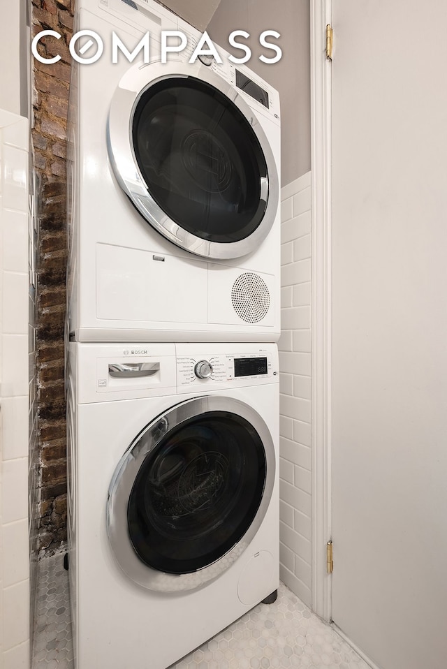 laundry area with stacked washing maching and dryer, tile patterned floors, laundry area, and tile walls