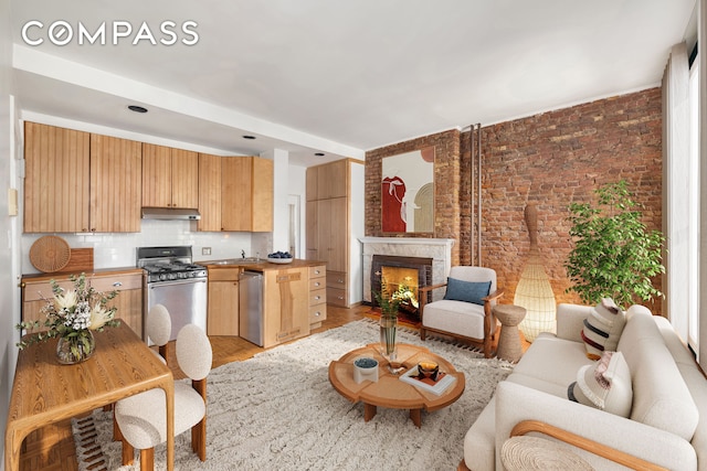 kitchen with a sink, dishwasher, backsplash, under cabinet range hood, and gas range oven