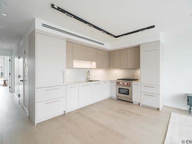 kitchen with modern cabinets, luxury stove, light countertops, light wood finished floors, and backsplash