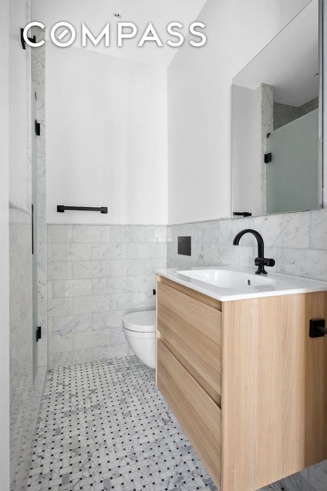 bathroom featuring vanity, toilet, tile walls, an enclosed shower, and a wainscoted wall