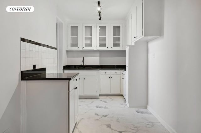 kitchen with dark countertops, marble finish floor, white cabinetry, and glass insert cabinets