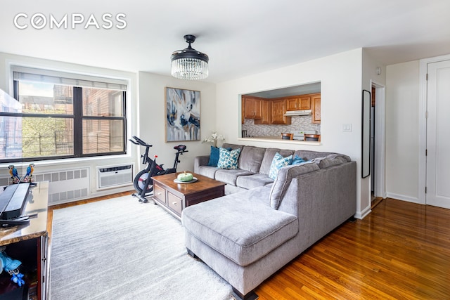 living area featuring baseboards, a wall unit AC, wood finished floors, and radiator