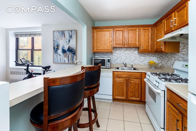kitchen with decorative backsplash, white appliances, light countertops, under cabinet range hood, and a sink
