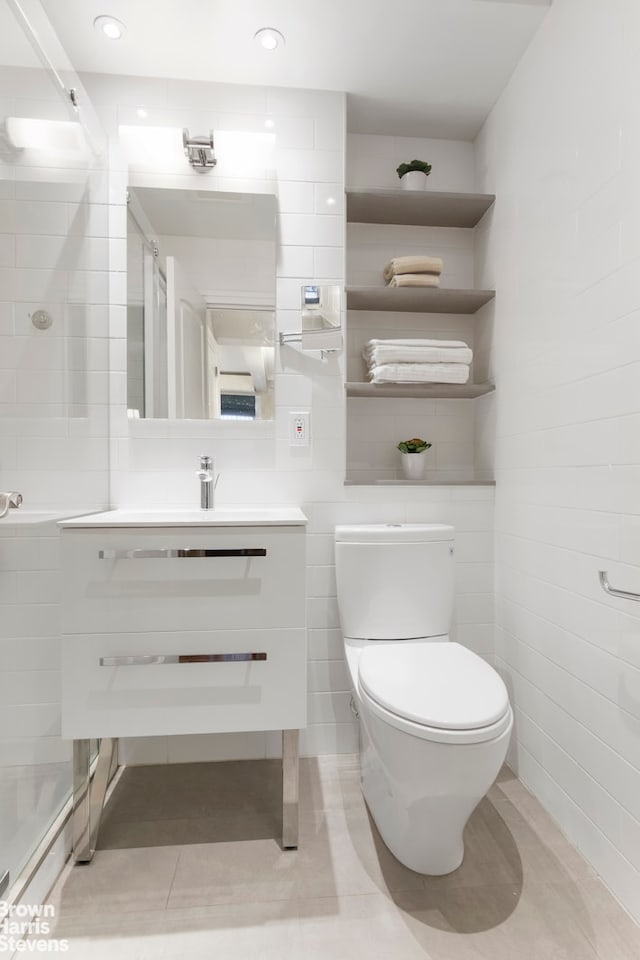 bathroom with walk in shower, vanity, toilet, tile patterned floors, and tile walls