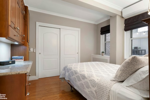 bedroom featuring a closet, ornamental molding, baseboards, an AC wall unit, and light wood-style flooring