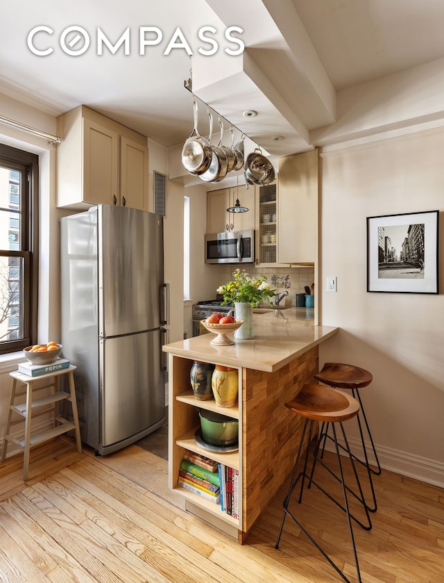 kitchen featuring a peninsula, a kitchen breakfast bar, light wood-type flooring, tasteful backsplash, and stainless steel appliances