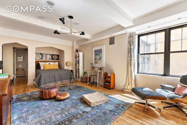 bedroom featuring visible vents, wood finished floors, beam ceiling, baseboards, and arched walkways